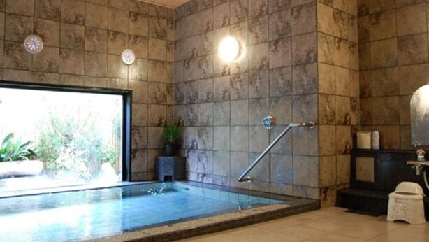 A spa area with a stone wall, a small pool, a clock, and a toilet. - Hotel Route Inn Nabari (Nabari)
