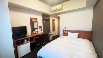 A hotel room with a bed, a desk with a computer, a television, and a mini-fridge.