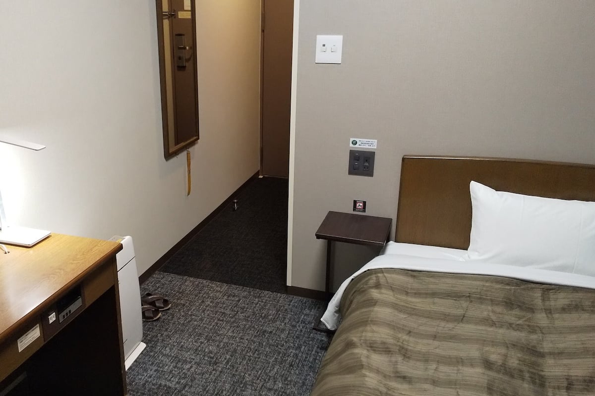 Ein Hotelzimmer mit Bett, Schreibtisch, Stuhl, Spiegel, Nachttisch und Teppichboden.