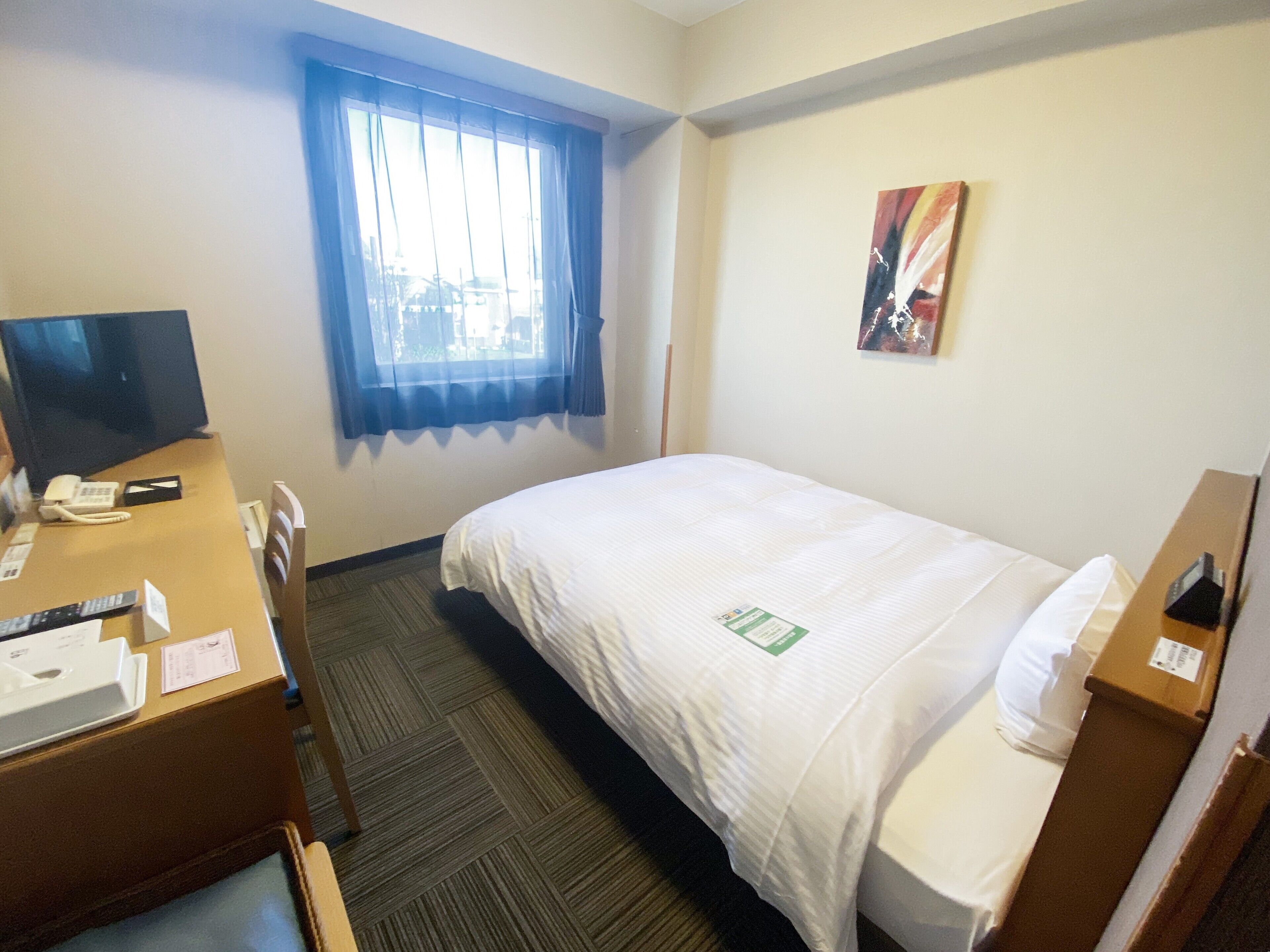 A hotel room with a bed, a desk with a telephone, a television, and a window with curtains.