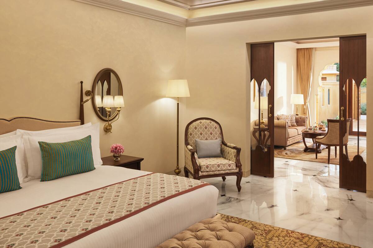 A hotel room with a large bed, a sitting area with a chair, a small table, and a view of the outside.