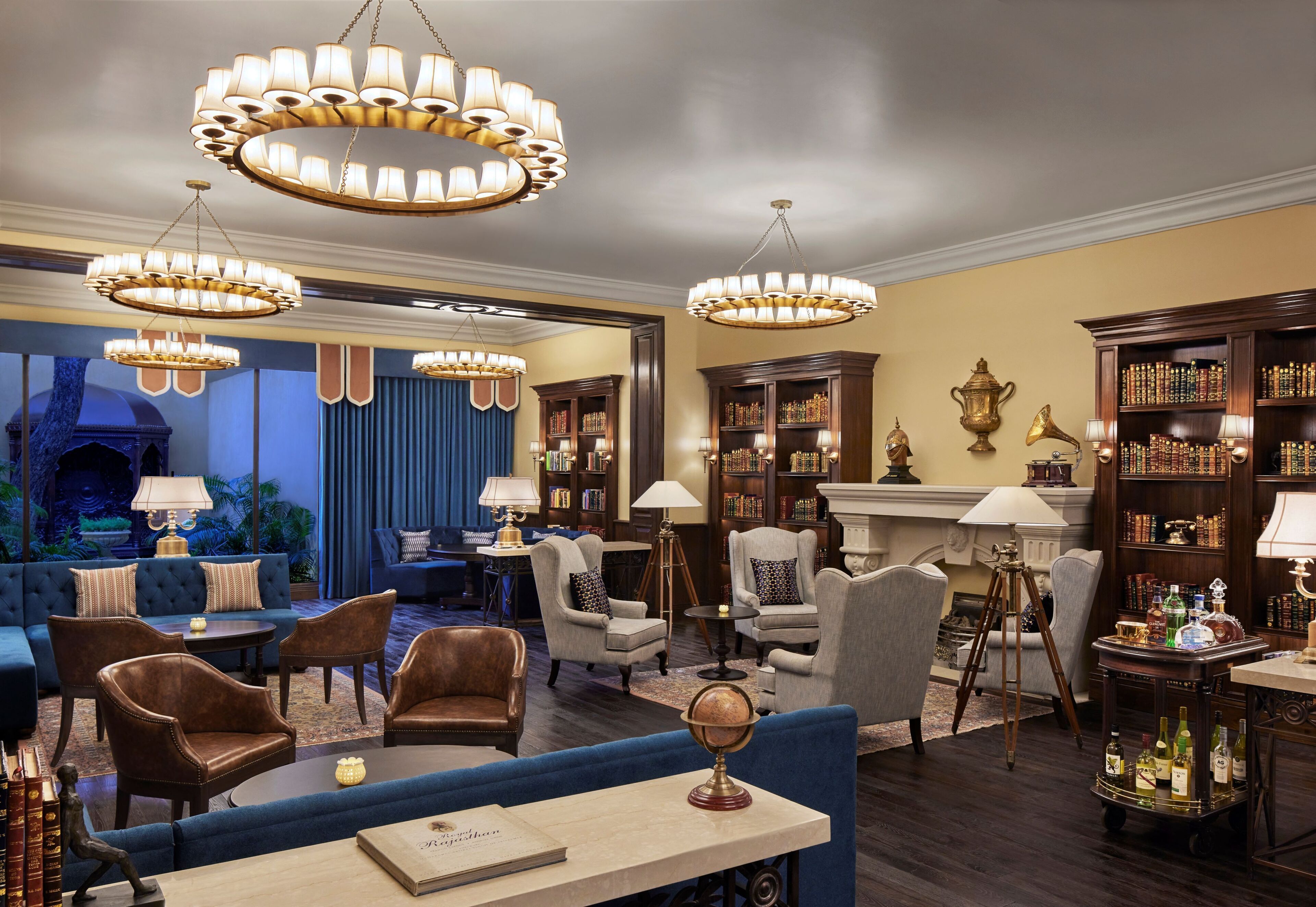 A spacious lounge with multiple seating areas, including sofas and armchairs, surrounded by bookshelves and a fireplace.