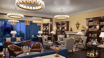 A spacious lounge with multiple seating areas, including sofas and armchairs, surrounded by bookshelves and a fireplace.