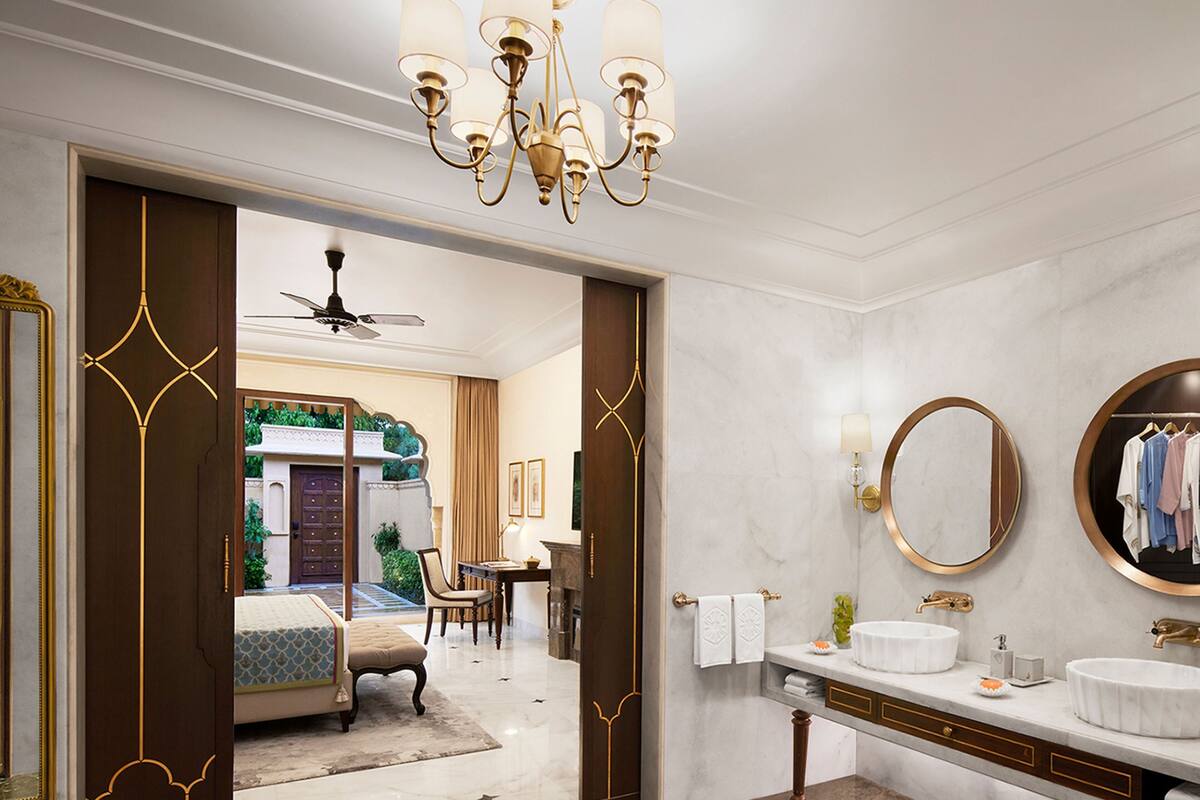 A luxurious bathroom with a marble floor, a large round mirror, a white sink, and a chandelier.