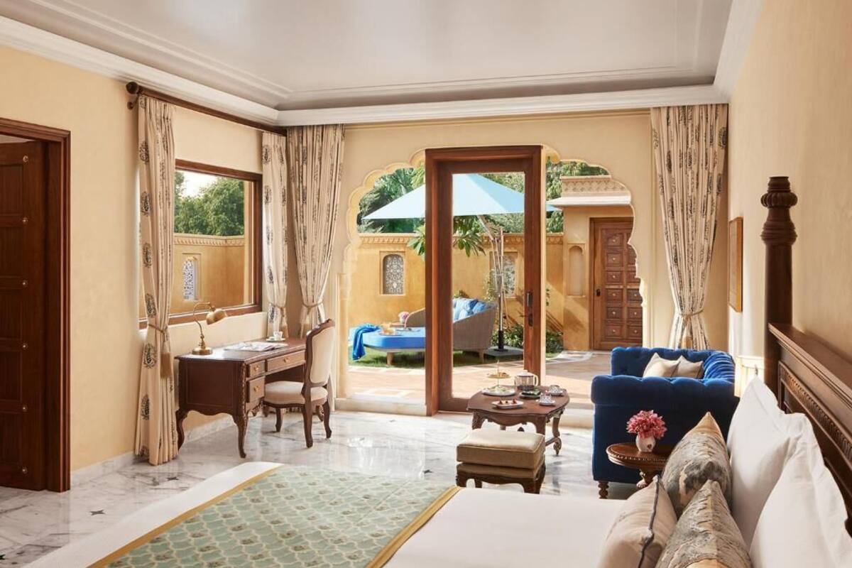 A hotel room with a bed, a desk, a chair, a sofa, and a view of an outdoor pool area.