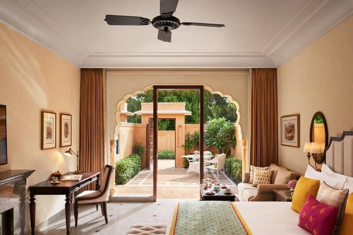 A hotel room with a bed, a desk, a chair, and a view of a courtyard.