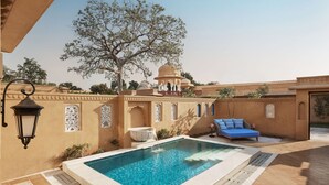 A pool area with a clear blue pool, a white water feature, and a blue sofa. - Sawai Man Mahal, Jaipur (Jaipur)
