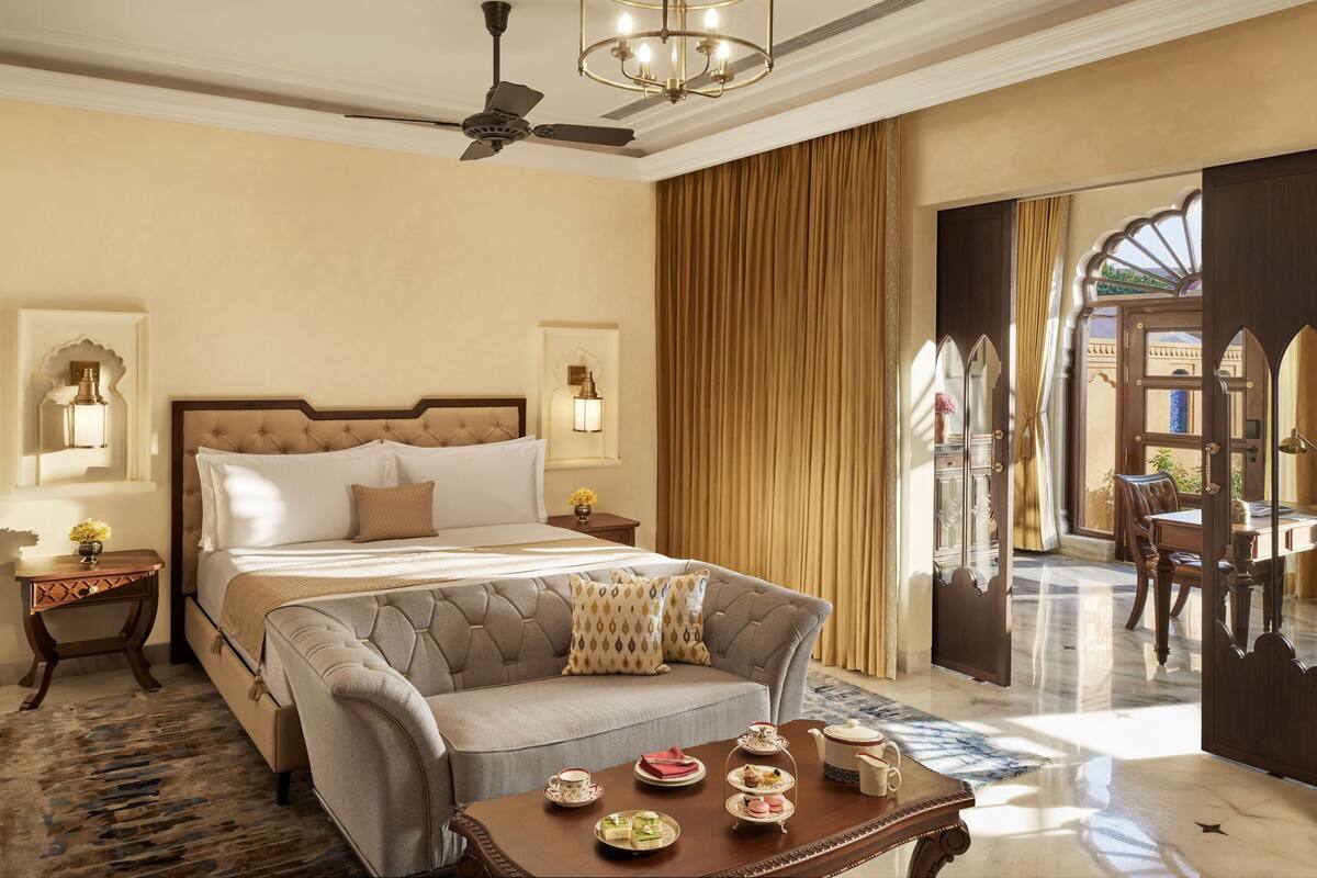 A hotel room with a large bed, a sofa, a table with tea sets, and a view of the outside through a door.