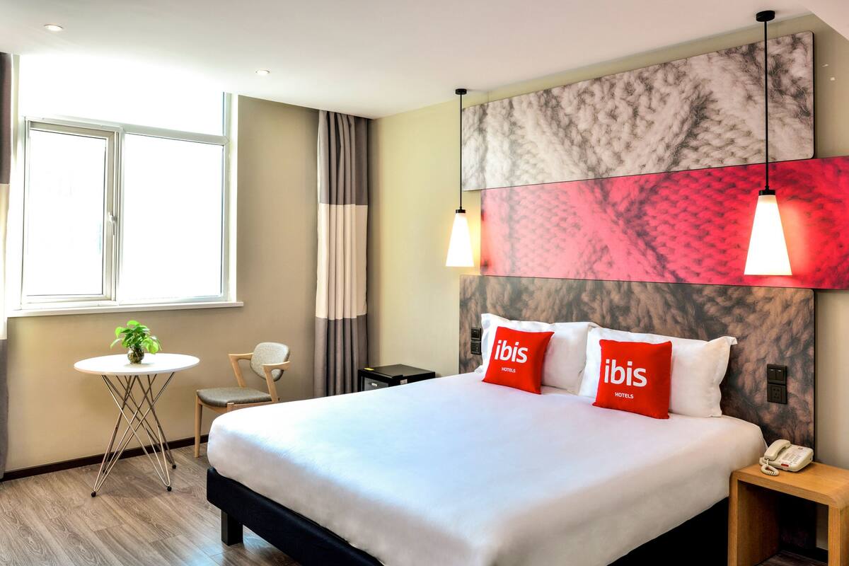Een hotelkamer met een groot bed, een tafeltje met een plant, een stoel en een nachtkastje met een telefoon.