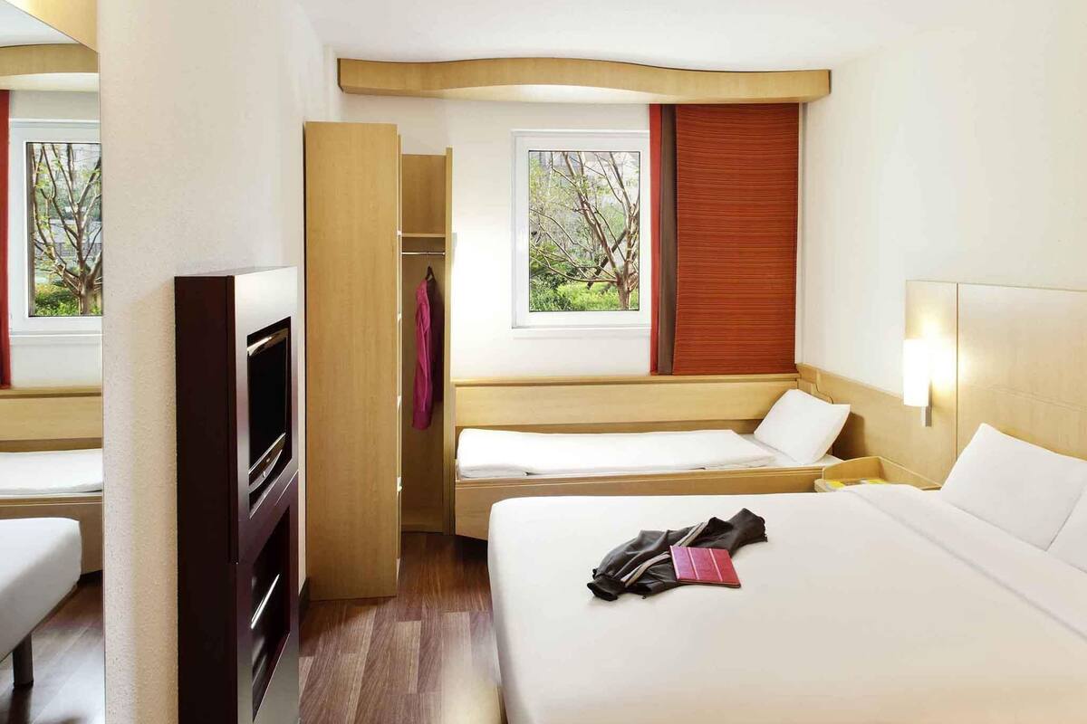 Een hotelkamer met een bed, een bureau, een kledingkast en een raam met uitzicht op bomen.