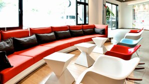 Un espace de détente moderne avec un canapé rouge, des tables blanches et des chaises colorées.