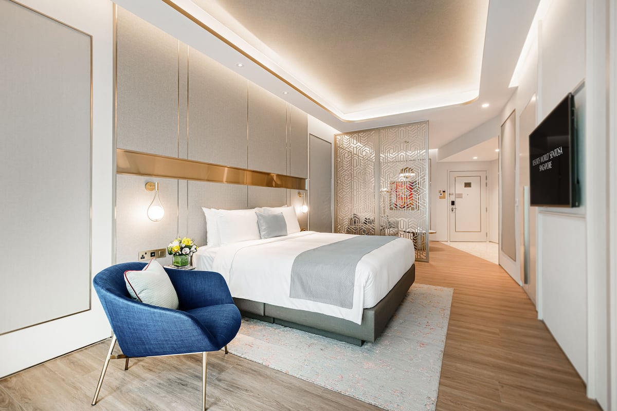 A modern hotel room with a large bed, a blue armchair, and a decorative partition.