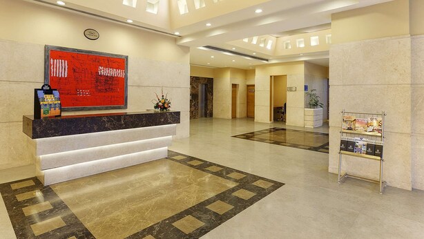 Uma área de recepção de hotel com um balcão de mármore, um letreiro vermelho com texto branco e um piso estampado.