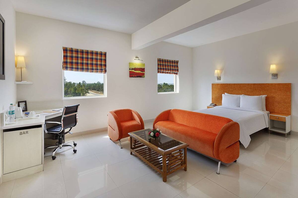 Una habitación de hotel con cama, escritorio, sillón, sofá y dos ventanas con cortinas.