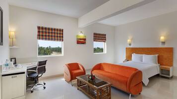 A hotel room with a bed, a desk, a chair, a sofa, and two windows with curtains.