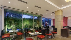 Um restaurante moderno com paredes de vidro, cadeiras vermelhas e vista para o verde lá fora.