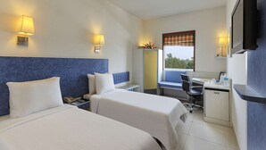 Quarto de hotel com duas camas, uma escrivaninha, uma cadeira, uma televisão e uma janela com vista.
