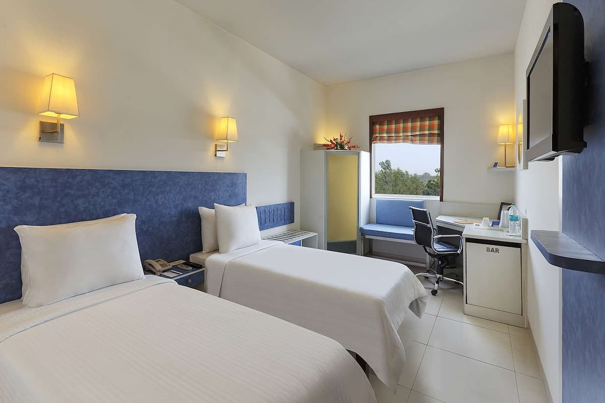 Habitación de hotel con dos camas, un escritorio, una silla, un televisor y una ventana con vistas.