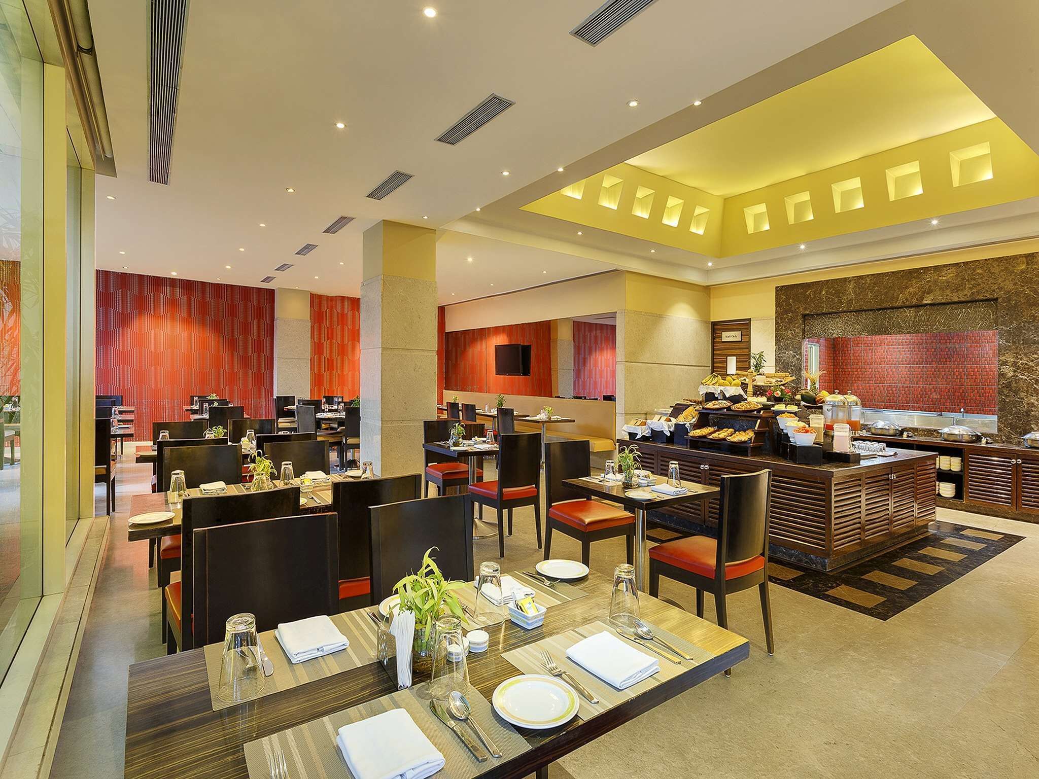 A modern hotel dining area with multiple tables, chairs, and a buffet setup.
