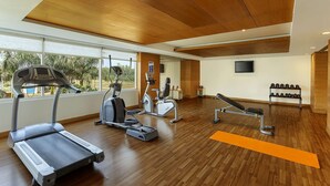 Academia moderna com equipamentos de ginástica, amplas janelas e piso de madeira.
