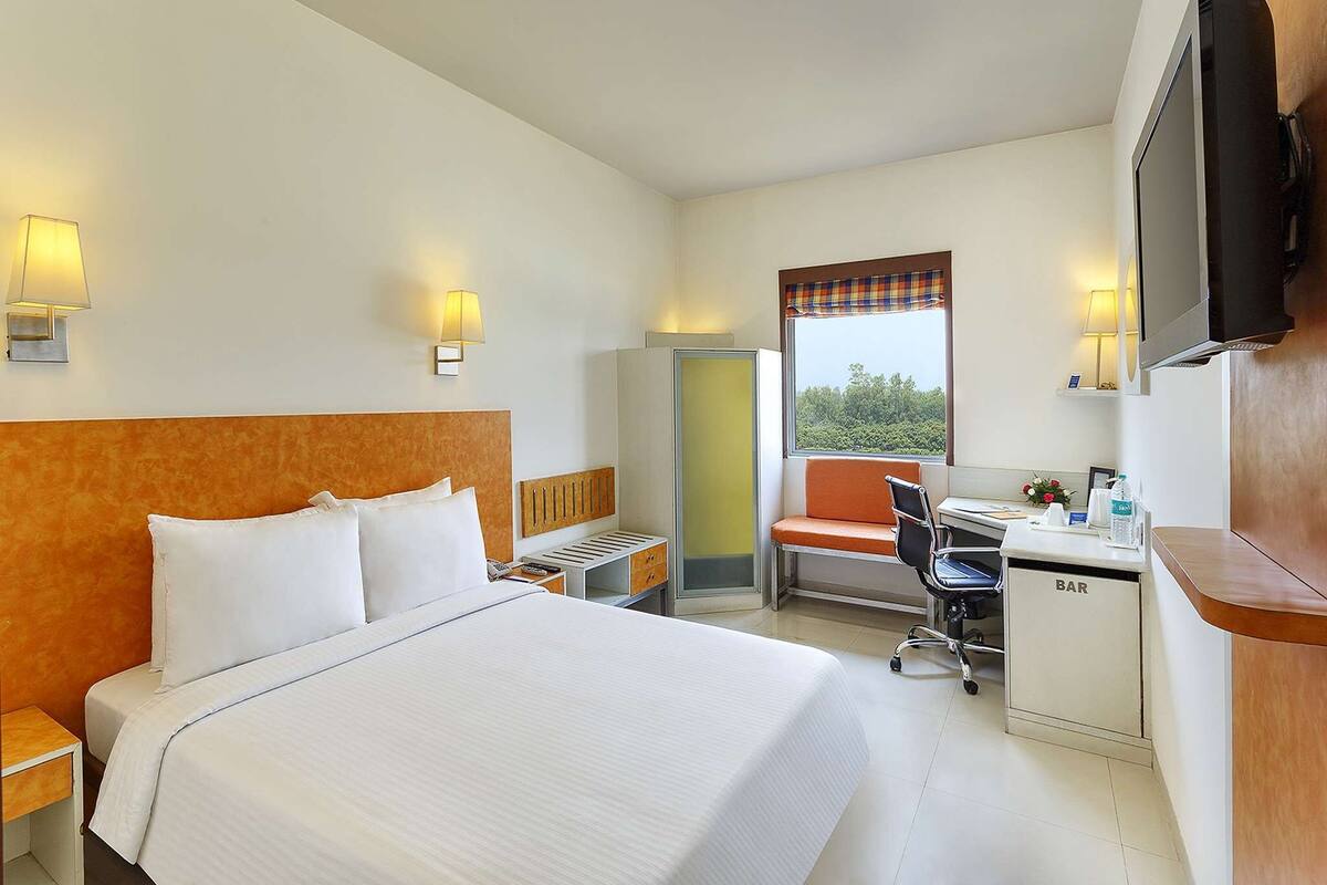 Habitación de hotel con una cama grande, un escritorio, una silla, un televisor y una ventana con vistas.