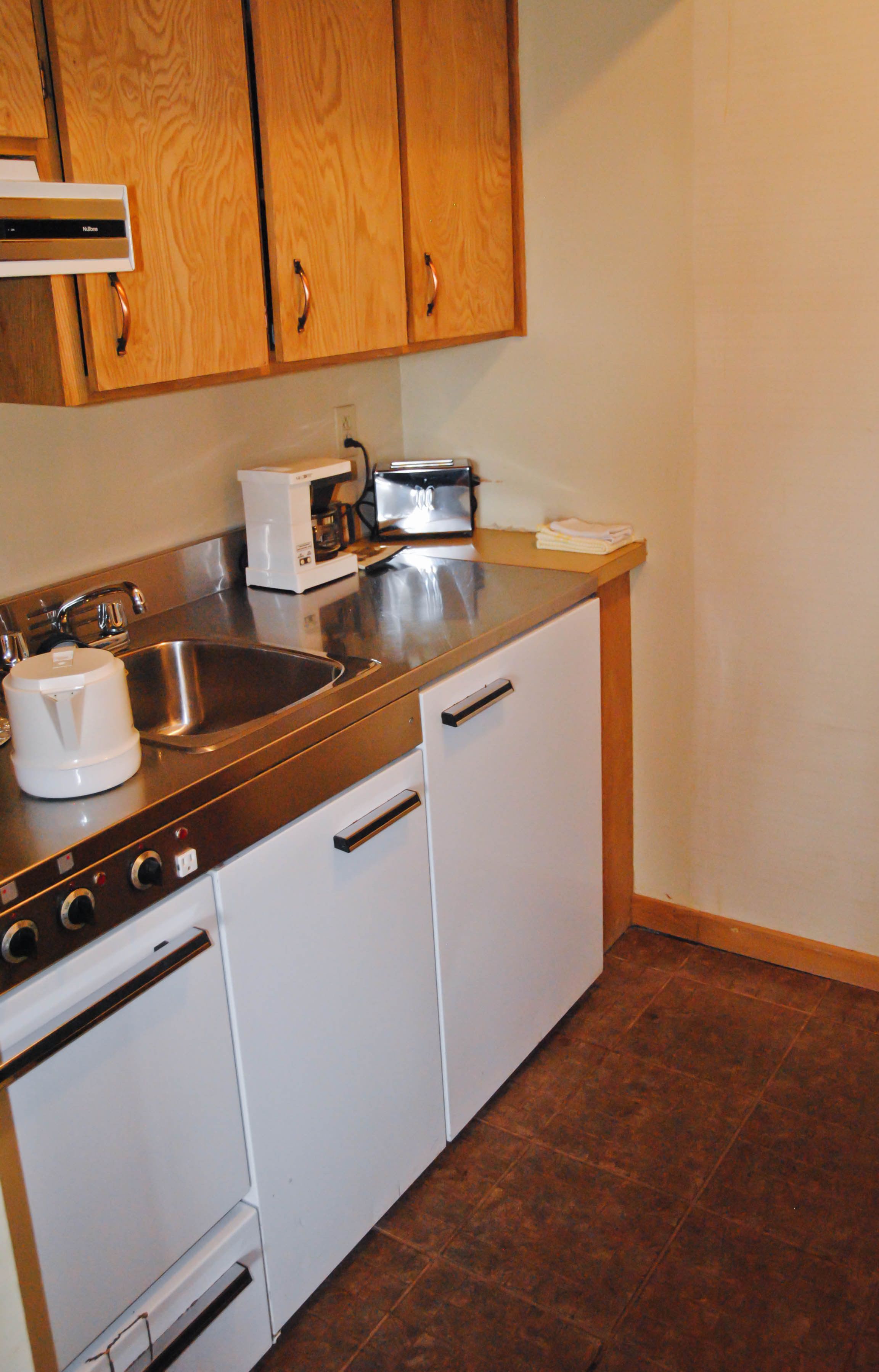 A kitchen with wooden cabinets, a stainless steel sink, a coffee maker, and a toaster.