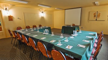 Un salón de conferencias con una larga mesa, sillas, una pantalla de proyector y una pizarra.