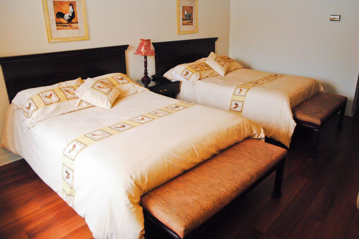 Una habitación de hotel con dos camas, una mesita de noche, una lámpara y un banco.