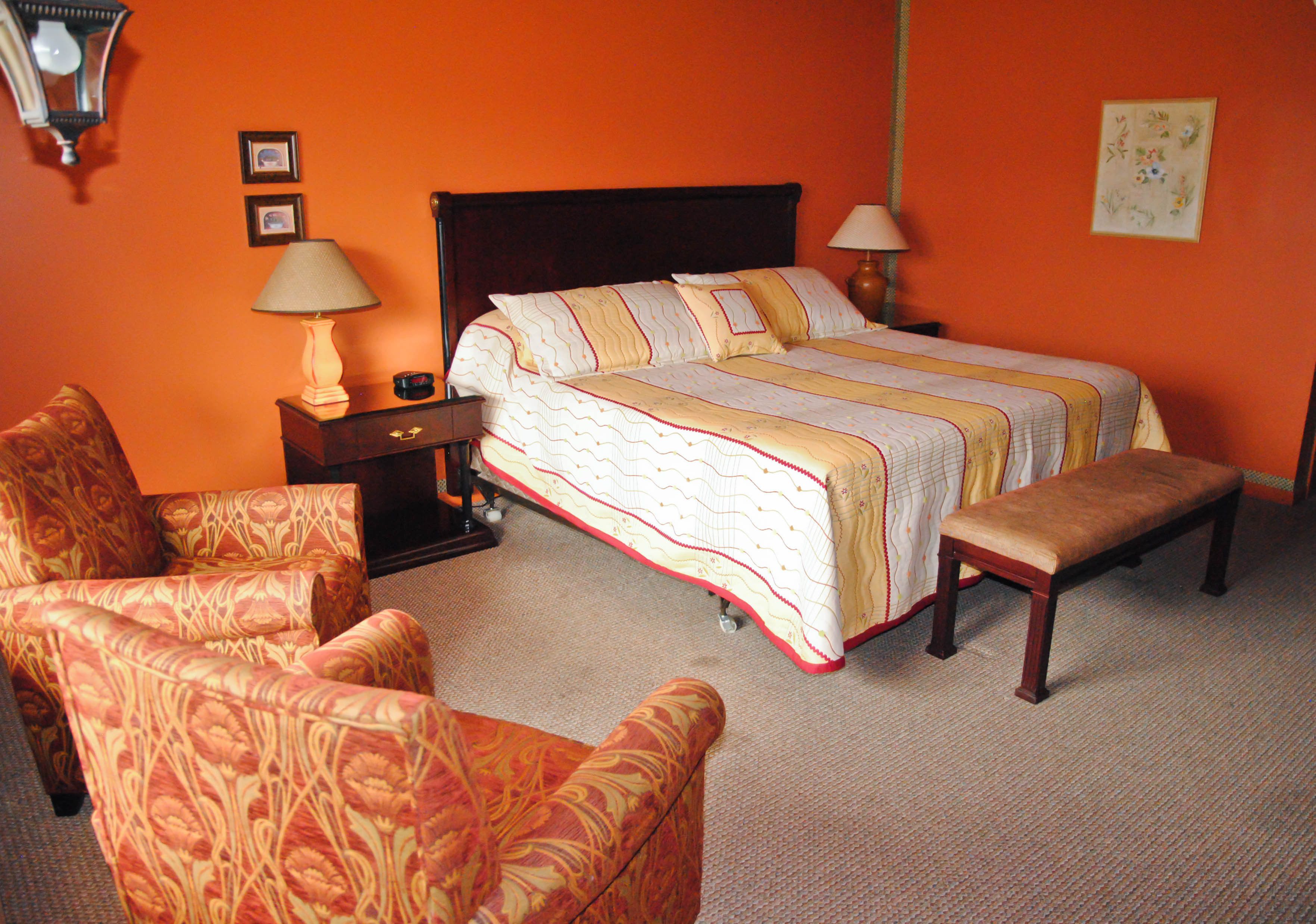 Una habitación de hotel con una cama grande, dos mesitas de noche, una silla y un banco.