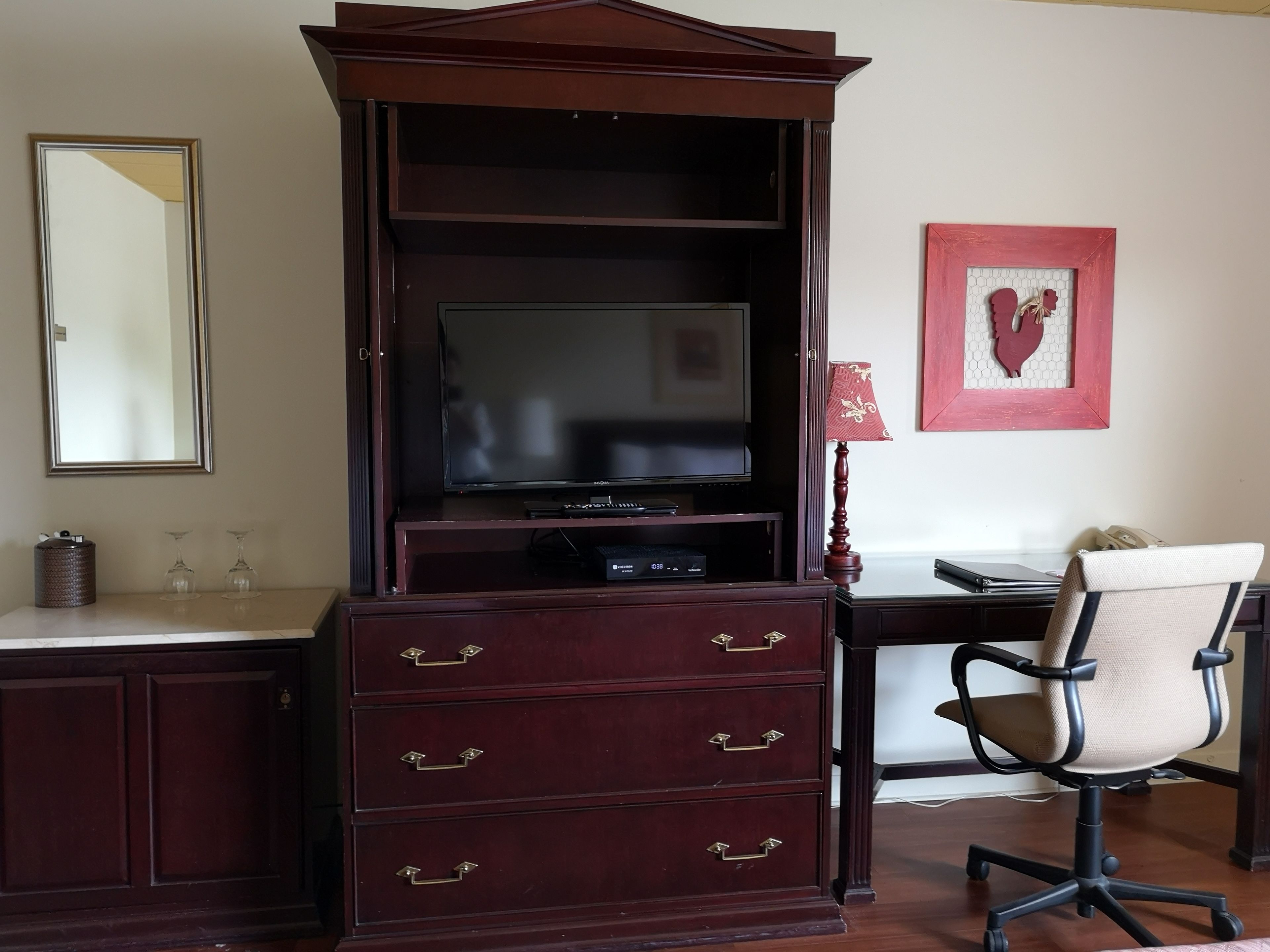 A dark wood entertainment center with a flat-screen TV, a red-framed picture, and a lamp.