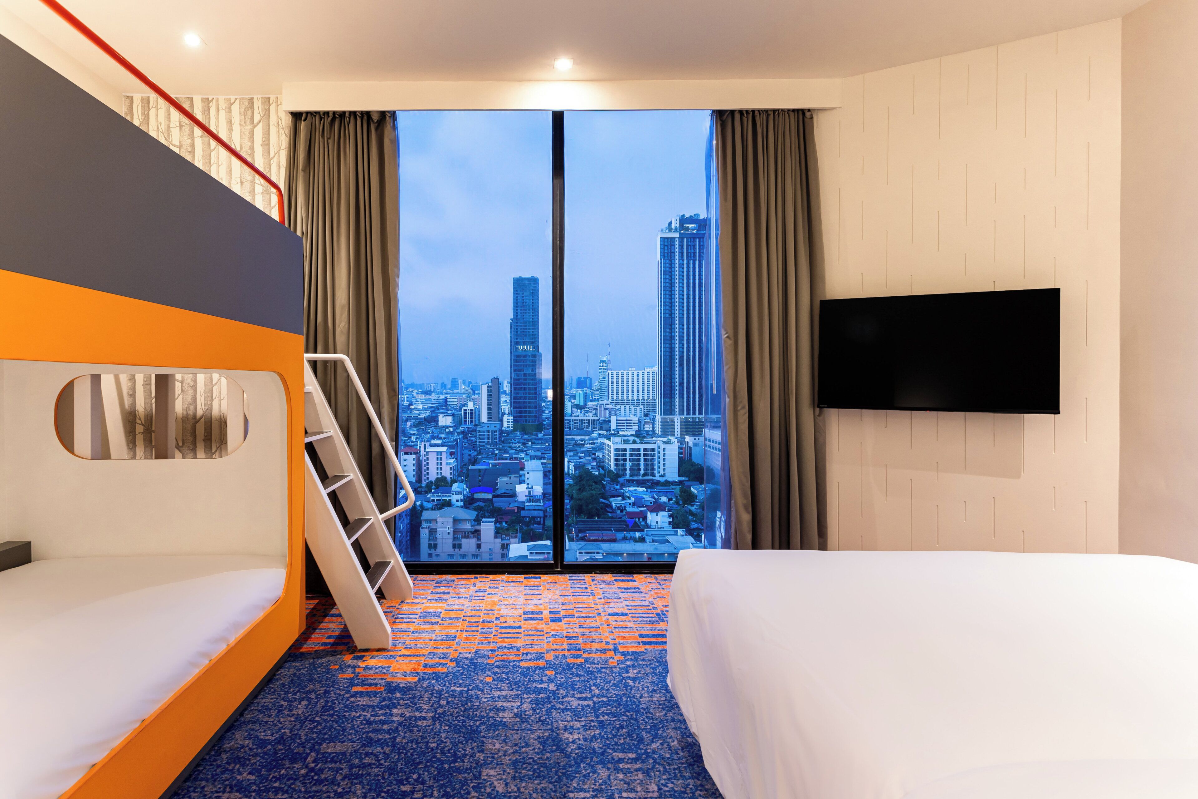 Quarto de hotel com vista para a cidade, uma cama, um sofá, uma televisão e uma escada.