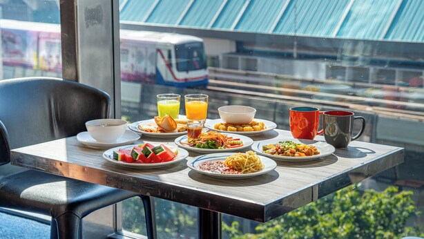 Taula de desjuni amb plats de menjar, un bol i dues tasses, amb vista a un tren i terrasses verdes.