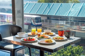A breakfast table with plates of food, a bowl, and two cups, overlooking a train and green roofs.