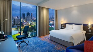 A hotel room with a large bed, a desk, a chair, and a view of a cityscape at dusk. - Holiday Inn Express Bangkok Siam by IHG (Bangkok)