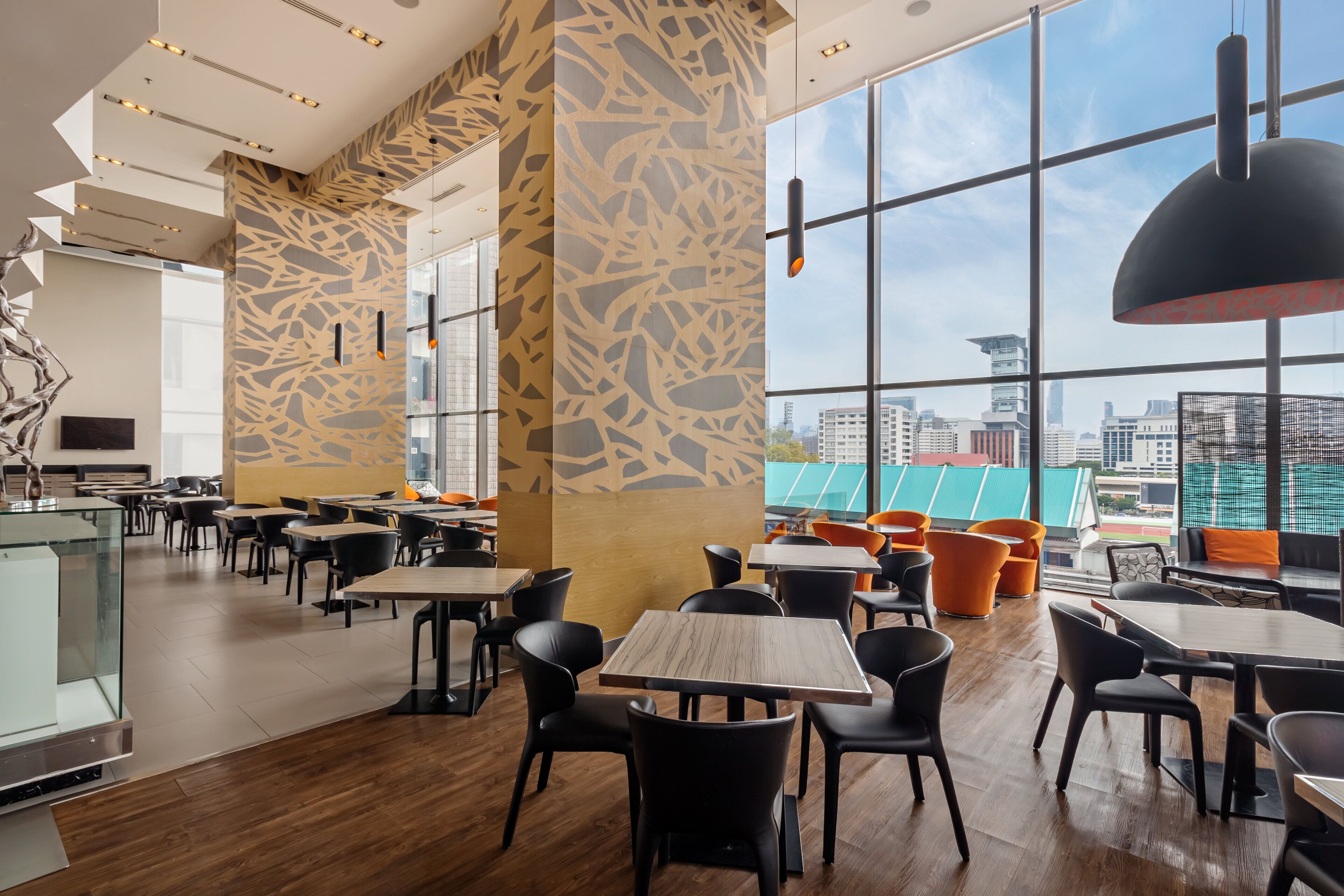 A modern restaurant interior with high ceilings, patterned walls, and large windows offering city views.