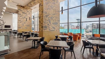 A modern restaurant interior with high ceilings, patterned walls, and large windows offering city views.