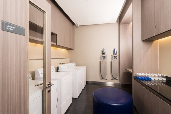 A laundry room with a sign, a row of washing machines, two dryers, and a water dispenser.