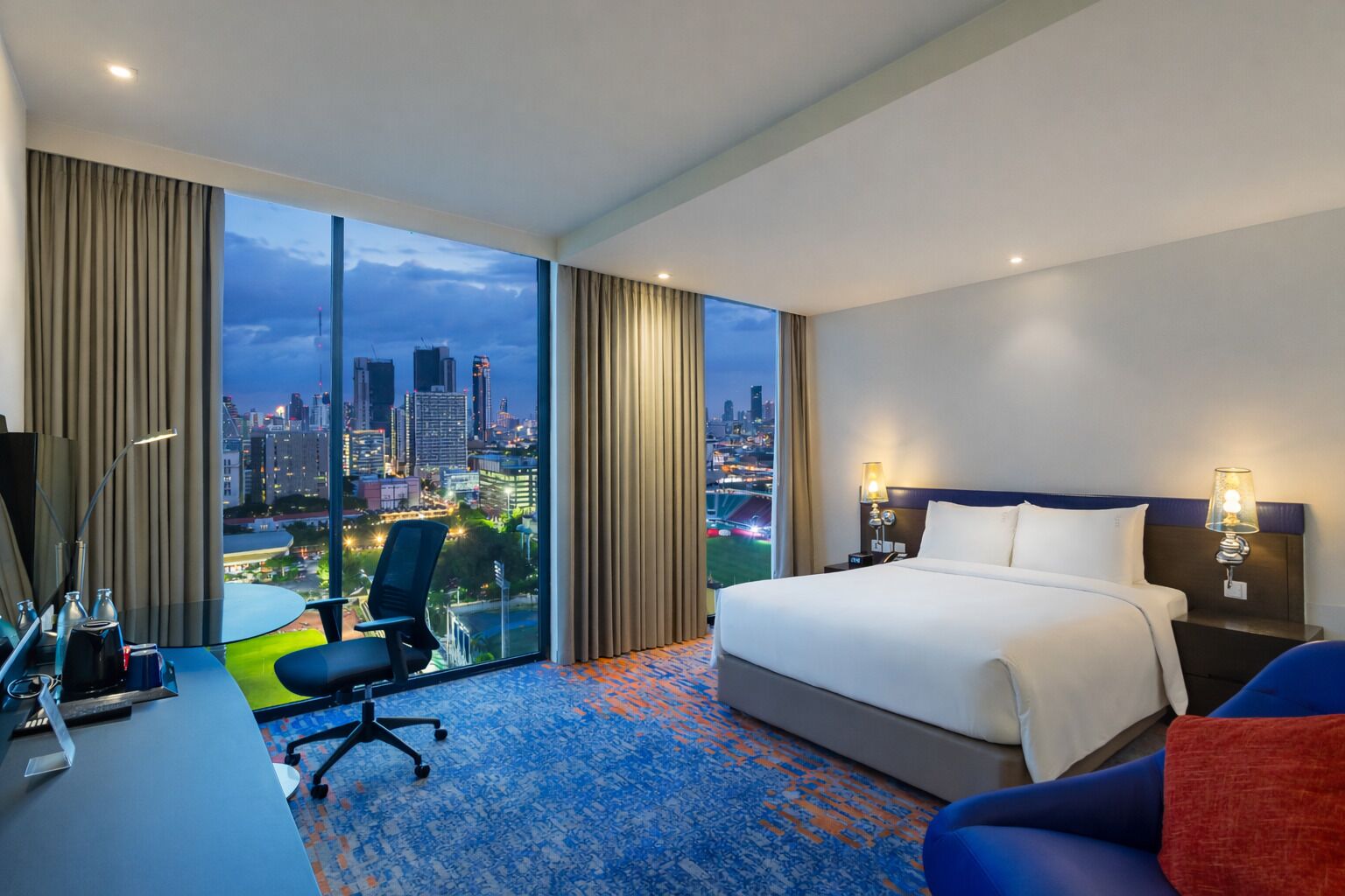 Une chambre d’hôtel avec un grand lit, un bureau avec une chaise, une télévision et une vue sur le paysage urbain.