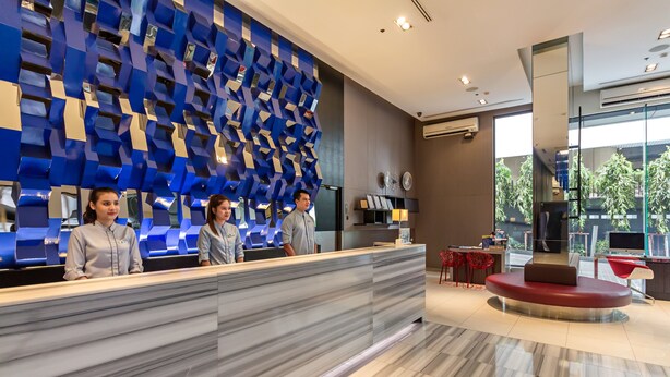 A reception area with a modern design, featuring a marble reception desk, a blue geometric wall, and a seating area with a red sofa. - Holiday Inn Express Bangkok Siam by IHG (Bangkok)