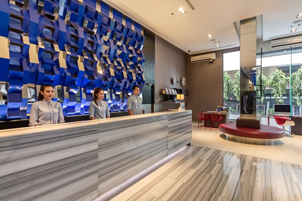 A reception area with a modern design, featuring a marble reception desk, a blue geometric wall, and a seating area with a red sofa. - Holiday Inn Express Bangkok Siam by IHG (Bangkok)