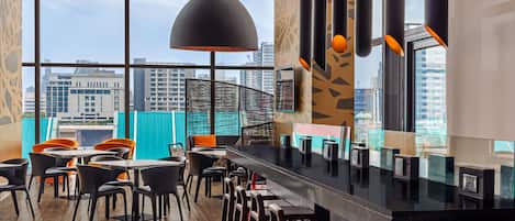 A modern bar area with high ceilings, large windows, and a view of the city skyline.
