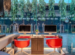 A modern indoor space with two computer monitors, a wooden table, and red chairs. - Holiday Inn Express Bangkok Siam by IHG (Bangkok)