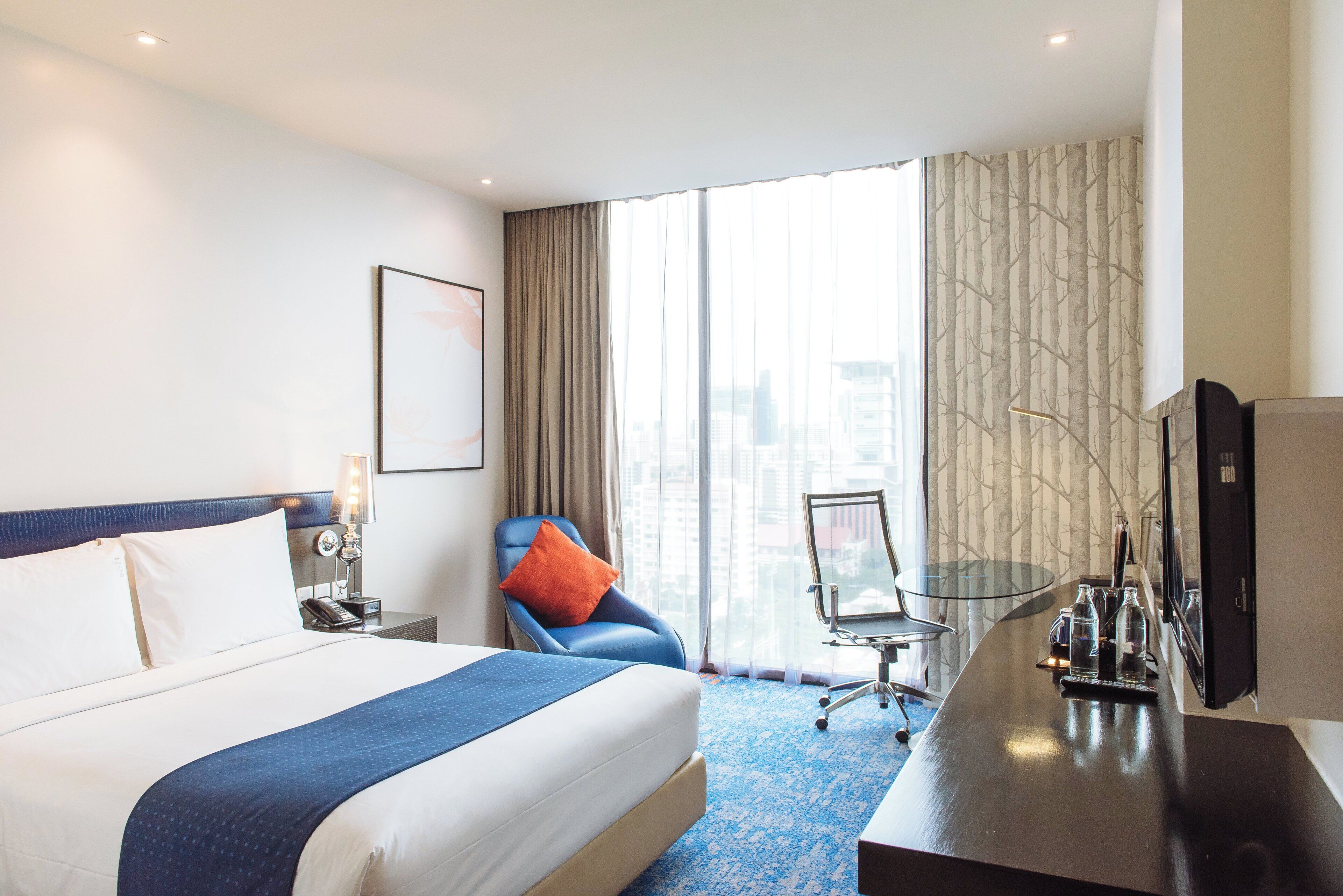 A hotel room with a bed, a desk, a chair, a TV, and a large window.