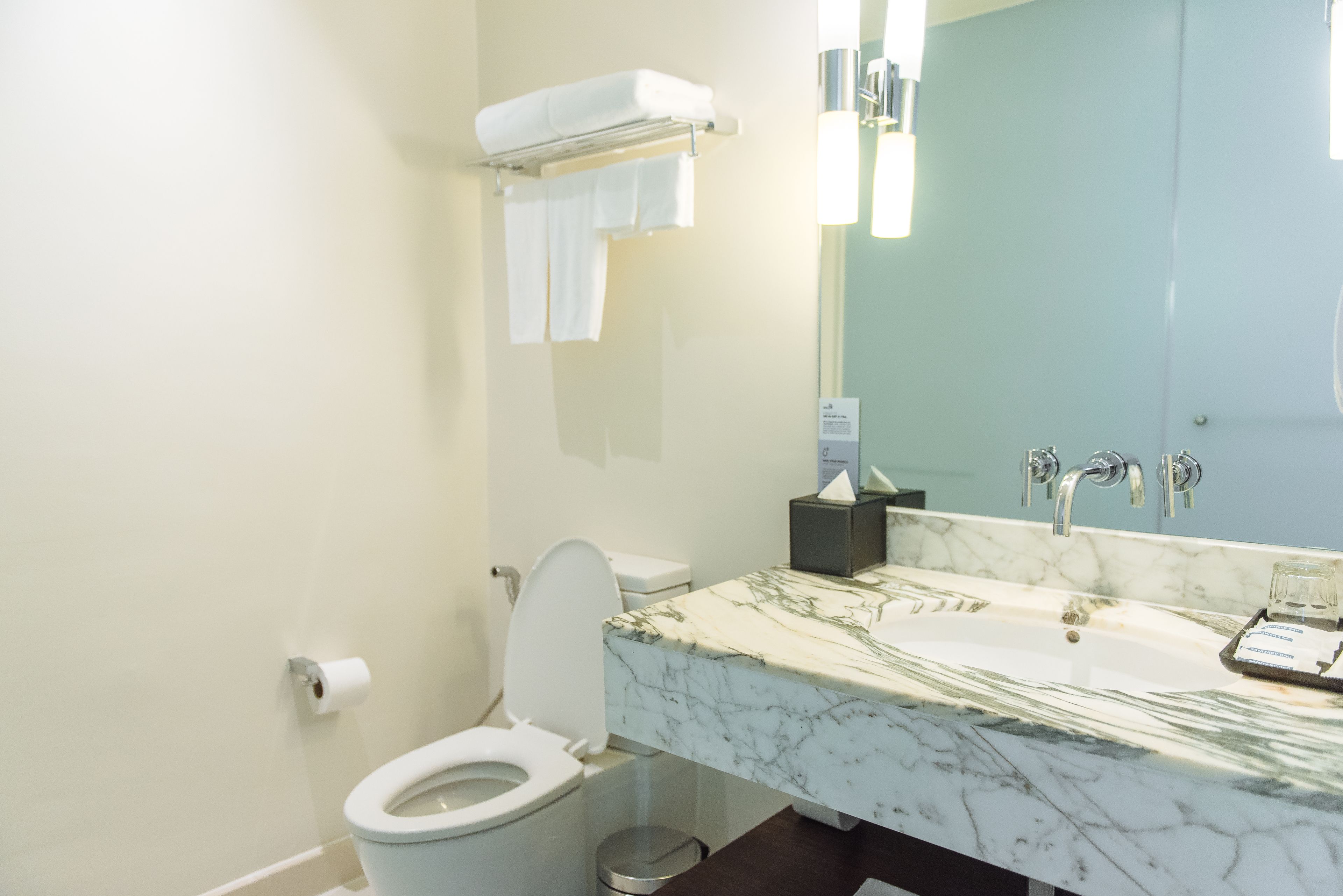 A modern bathroom with a white toilet, a marble sink, and a large mirror.