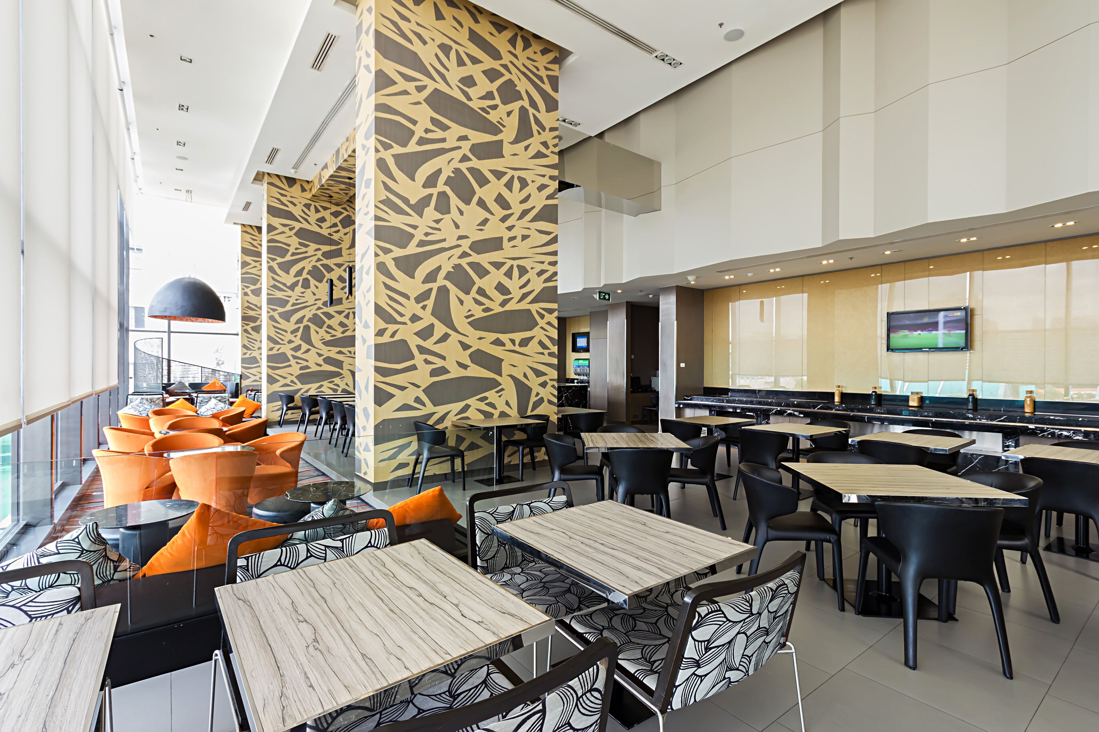 A modern restaurant with high ceilings, patterned walls, and a variety of seating arrangements including tables and chairs.