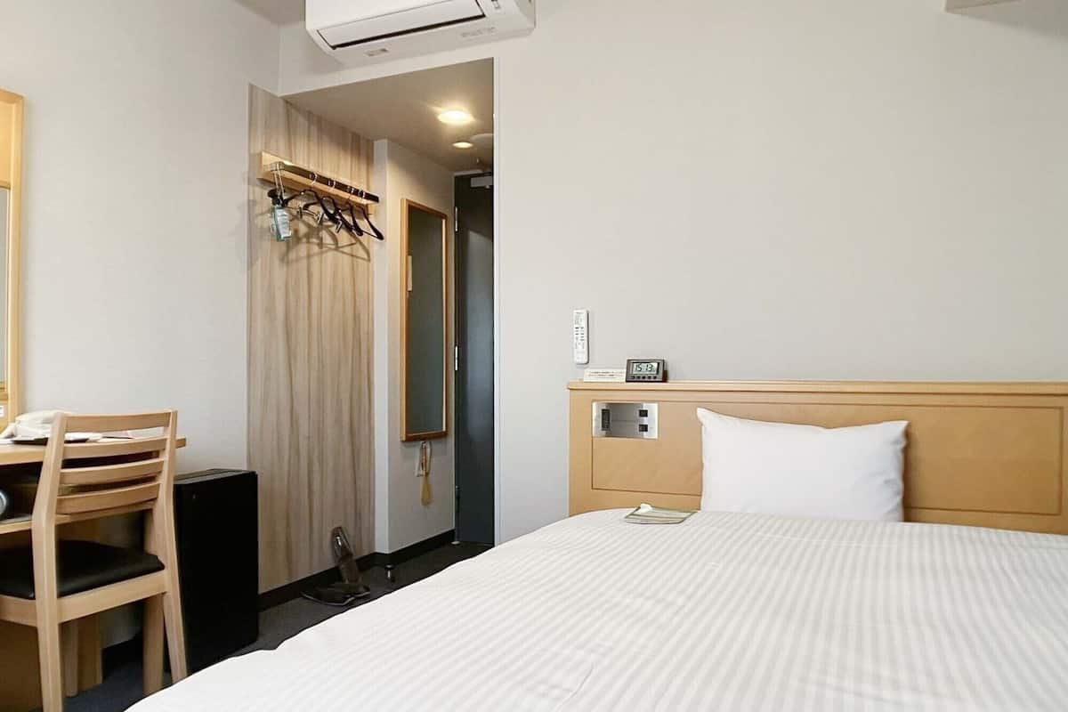 Ett hotellrum med en säng, ett skrivbord, en stol, en garderob och en spegel.