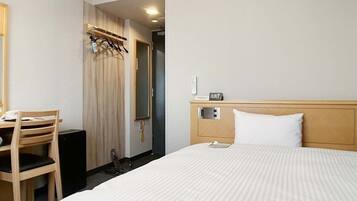 Una habitación de hotel con una cama, un escritorio, una silla, un armario y un espejo.
