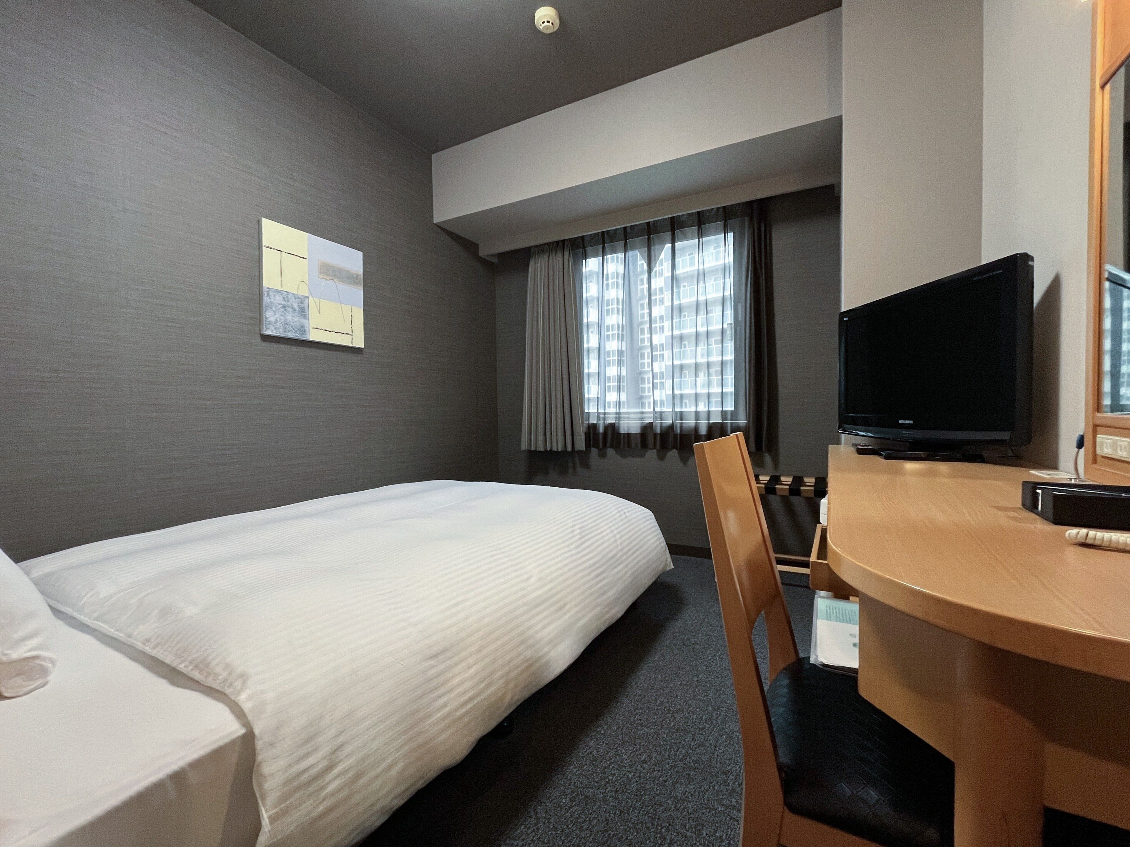 Una habitación de hotel con una cama individual, un escritorio con silla, un televisor y una ventana con cortinas.