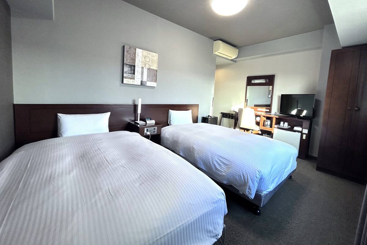 A hotel room with two beds, a desk, a chair, a TV, and a mirror.