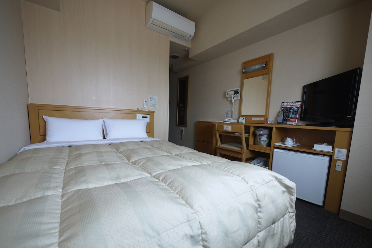 A hotel room with a large bed, a desk with a computer, a television, and a small refrigerator.